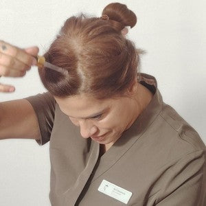 Revi places drops from a glass dropper onto the skin of a parting