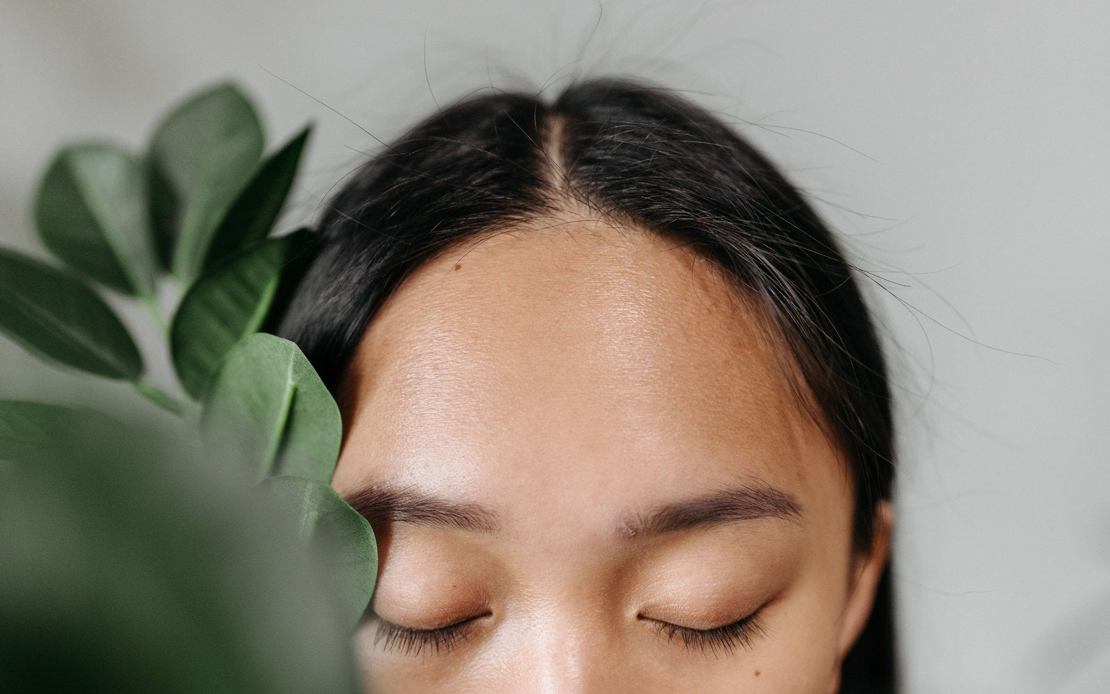 A woman with dark hair and closed eyes, the skin of her scalp visible along a straight parting